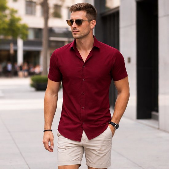 Man met korte mouwen bordeauxrood overhemd, beige shorts, zonnebril en horloge.