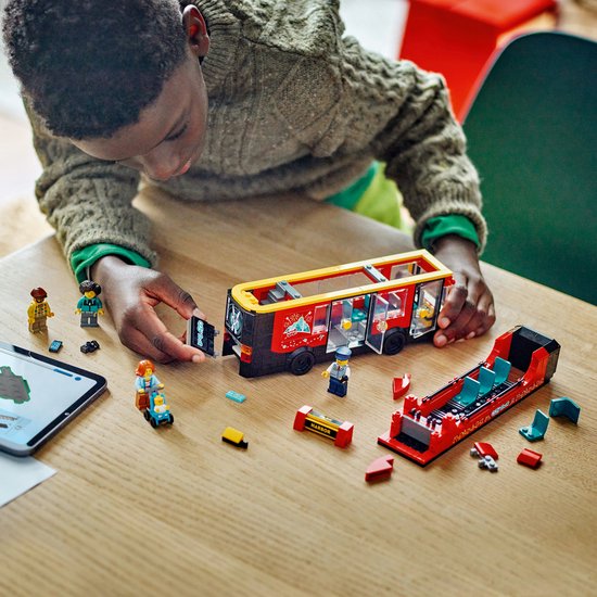 Jongen bouwt aan rode LEGO dubbeldekker bus met twee verdiepingen, met losse onderdelen.