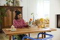 Une femme assise à une table construit un chrysanthème Lego. Les fleurs sont orange et rouges.