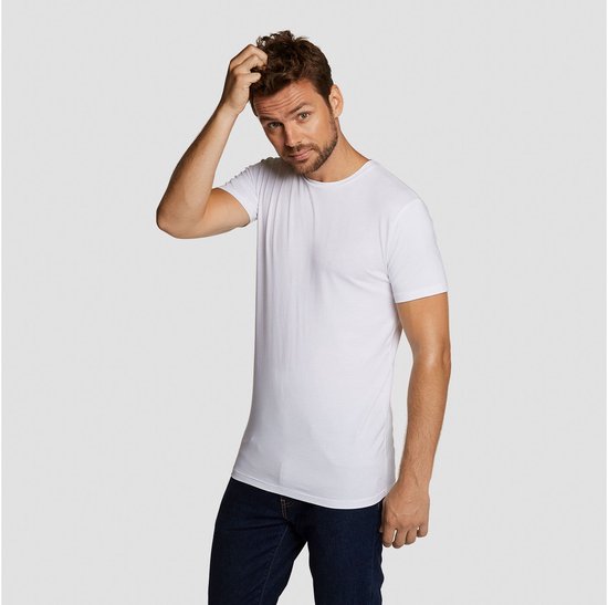 Man met donkere jeans, witte ronde hals t-shirt. Hij krabt aan zijn hoofd.