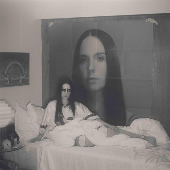 Vrouw met donker haar en make-up ligt op een bed, voor een poster van haar gezicht.