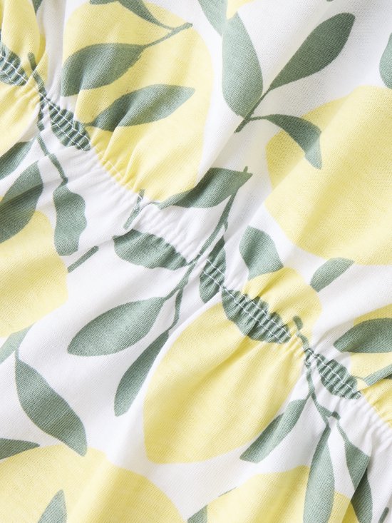 Witte stof met een all-over print van gele citroenen en groene bladeren. Elastische zoom.