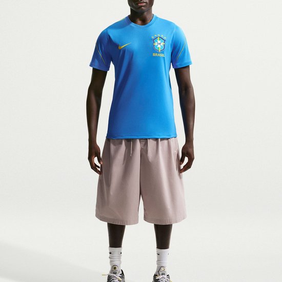 Man in blauw sportshirt met "CBF BRASIL" logo en beige korte broek.
