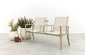 Beige aluminium tuinbank met stoffen zittingen en middenplateau, met planten en een lantaarn ernaast.