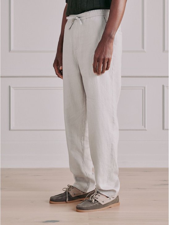 Man met donkere huidskleur, draagt een crème linnen broek met trekkoord en donkergroene trui.