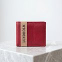 Lundholm portemonnee van rood leer met band met "LUNDHOLM"-tekst, op een marmeren ondergrond.