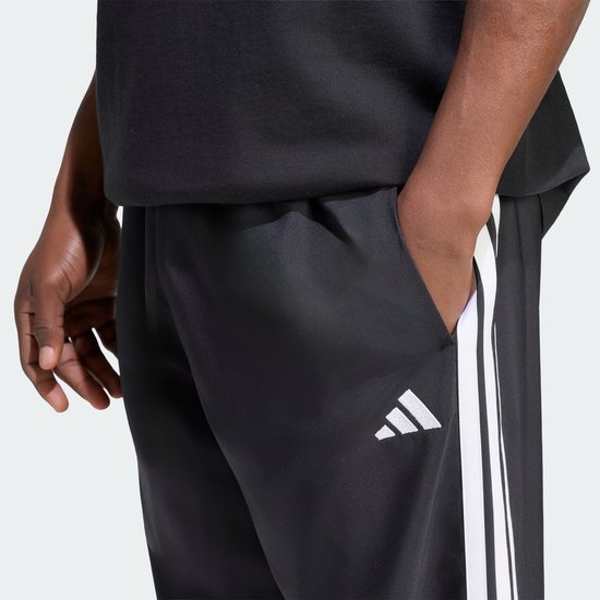 Close-up van een zwarte sportbroek met witte Adidas strepen en Adidas logo.