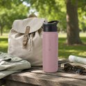 Roze 500ml drinkfles met zwarte rietjesdop, naast een rugzak op een picknicktafel.