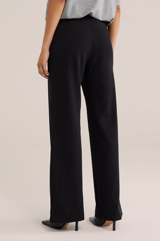 Zij-aanzicht van de achterkant van een zwarte jersey broek met regular fit, gedragen door een model met hakken.