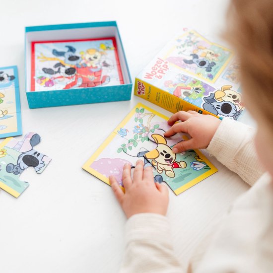 Handen van een kind dat een puzzelstukje van Woezel en Pip op de juiste plek legt. De puzzel is van 4 stukjes.