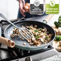 Lichtblauwe koekenpan met gebakken champignons. De tekst 'Coating versterkt met diamanten' en 'Bestand tegen metalen spatels' staat in de hoek.