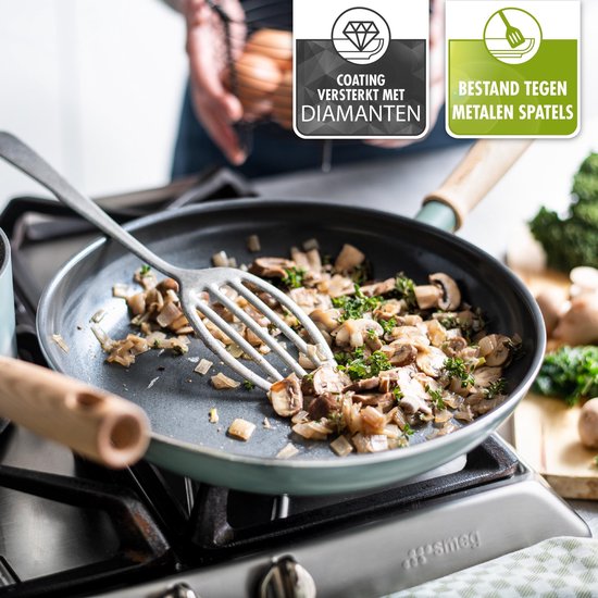 Lichtblauwe koekenpan met gebakken champignons. De tekst 'Coating versterkt met diamanten' en 'Bestand tegen metalen spatels' staat in de hoek.
