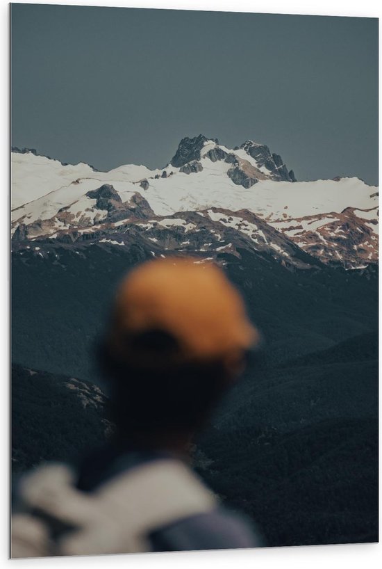 Dibond - Man met een Gele Pet Kijkend naar Besneeuwde Bergen - 80x120cm Foto op Aluminium (Wanddecoratie van metaal)