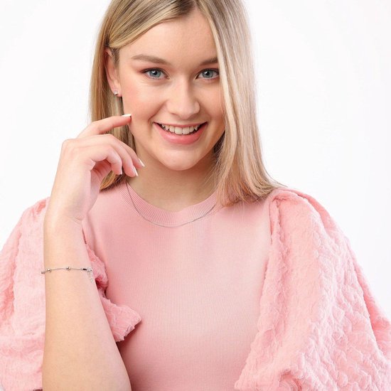 Vrouw met blonde haren in roze trui, draagt zilverkleurige slangenketting en armband