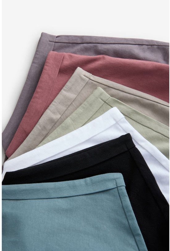 Detail van de zomen van meerdere effen T-shirts: zwart, wit, beige, lichtgroen, oudroze en grijs.