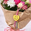 Gele hartjes bedel met lachend gezicht aan een boeket bloemen.