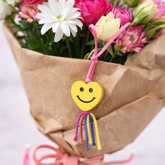 Gele hartjes bedel met lachend gezicht aan een boeket bloemen.