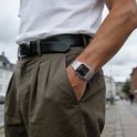Bras portant une montre argentée avec bracelet métallique, cadran noir, heure analogique et numérique, avec un t-shirt blanc et un pantalon marron.