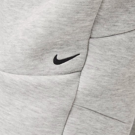 Close-up van de grijze Nike joggingbroek met een zwart Nike swoosh-logo.