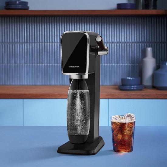 Zwarte bruiswatermachine met belletjes in de fles, naast een glas cola met ijs.