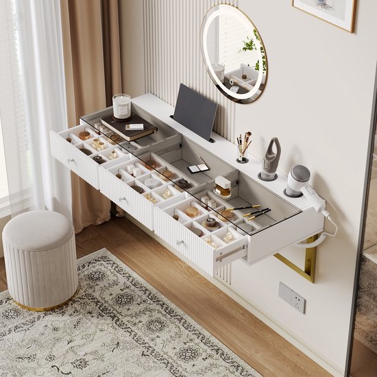 Coiffeuse blanche avec plateau en verre, trois tiroirs à rainures verticales, supports muraux dorés et compartiments internes pour le maquillage.