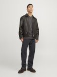 Model draagt losse, zwarte jeans met leren jack.
