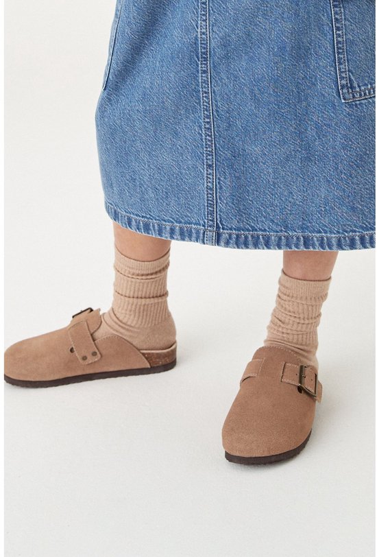 Meisje met bruine suède klompen, beige sokken en een spijkerrok.