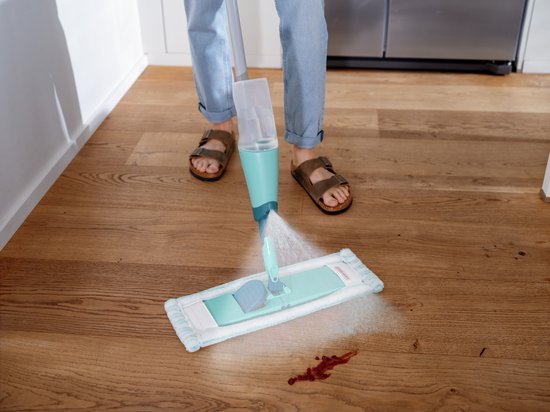 Vrouw poetst rode vlek op houten vloer met Leifheit Easy Spray XL vloerwisser.