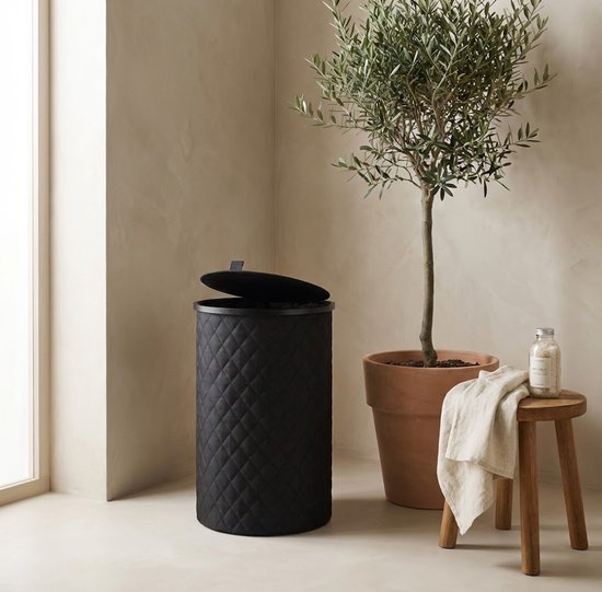 Zwarte, ronde wasmand met ruitpatroon, naast een pot met olijfboom.