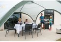 Een familie geniet van een maaltijd onder een Coleman partytent, met een barbecue ernaast.