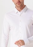 Man met kort bruin haar draagt een wit overhemd met lange mouwen en een grijze broek.