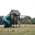 Groen speeltoestel met huisje, dubbele glijbaan, buisglijbaan en schommels.
