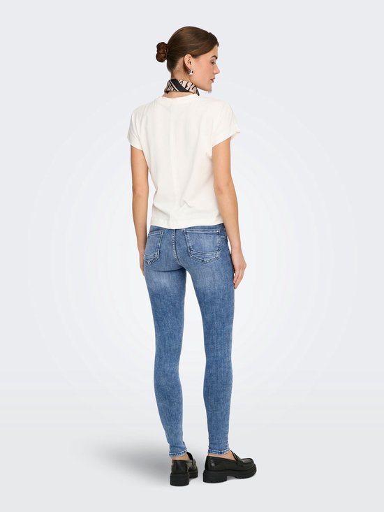 Model in lichte spijkerbroek en crèmekleurige top, van achteren gezien.