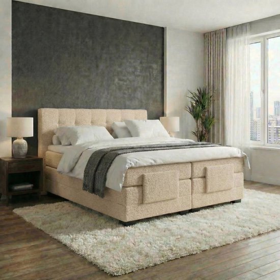 Een opgemaakt tweepersoonsbed met een teddy beige boxspring en hoofdbord, witte lakens en een grijze plaid. Een grote witte vloerkleed ligt ervoor.