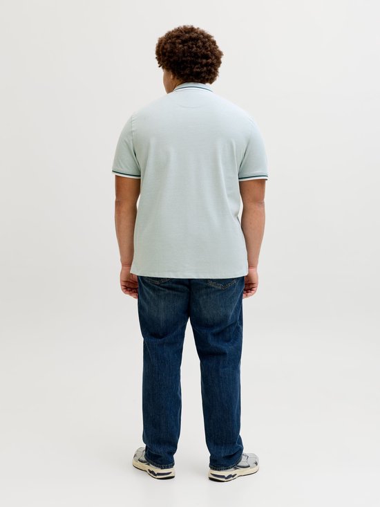 Man van achteren gezien, draagt een lichtgroene polo met groene en witte streepjes op de mouwen en een spijkerbroek.