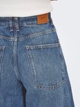 Close-up van de achterkant van een wijde, middendonkere spijkerbroek met hoge taille. Bruin leren label met 'ONLY' erop.