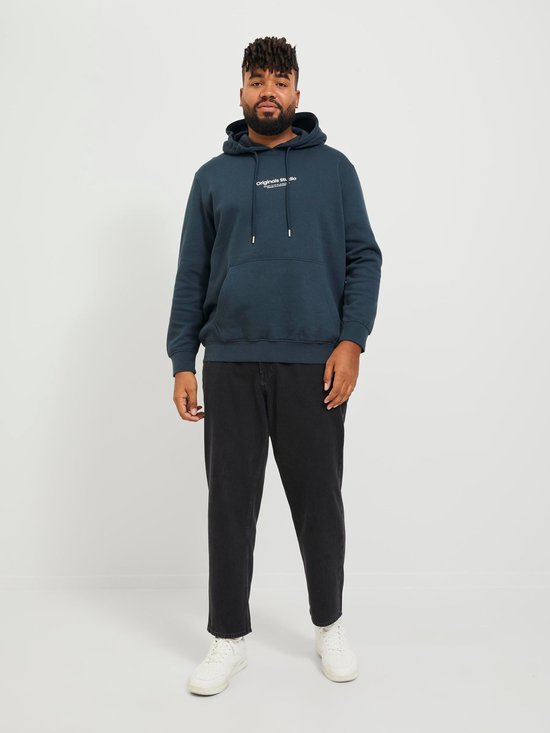 Man met donkere huid draagt een donkerblauwe hoodie met witte tekst en een zwarte jeans.