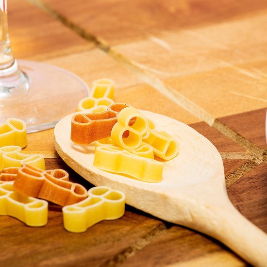 Houten lepel met naturel en bruine fallusvormige pasta, met meer pasta ernaast.