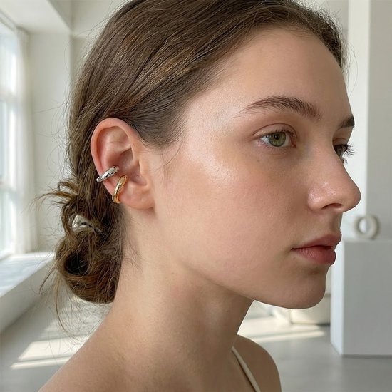 Close-up van een vrouw die zilverkleurige en goudkleurige ear cuffs draagt aan één oor.