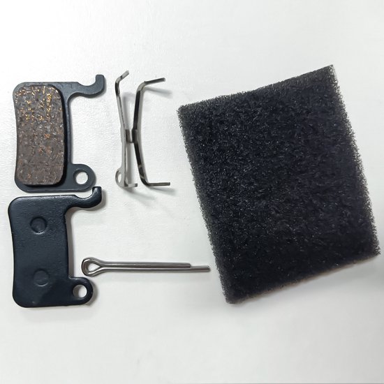 Twee zwarte remblokken, een metalen veer en een pen op een witte ondergrond.