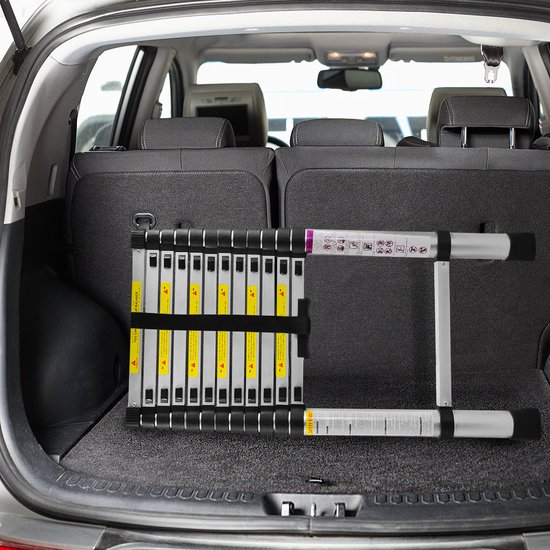 Gevouwen aluminium ladder in de kofferbak van een auto, met waarschuwingsstickers.