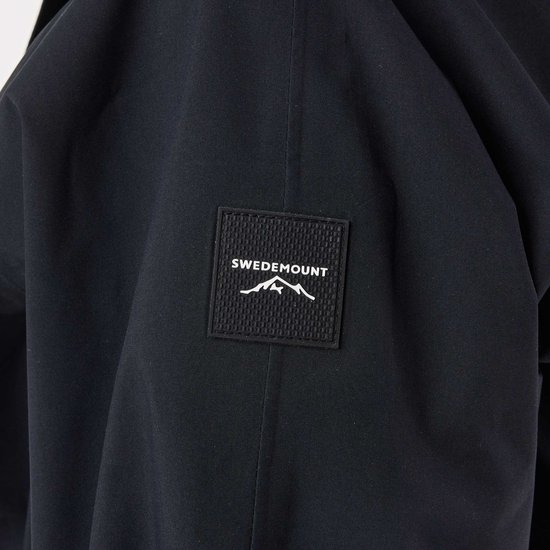 Détail d'un manteau noir avec un écusson logo représentant 'SWEDEMOUNT' et une montagne.