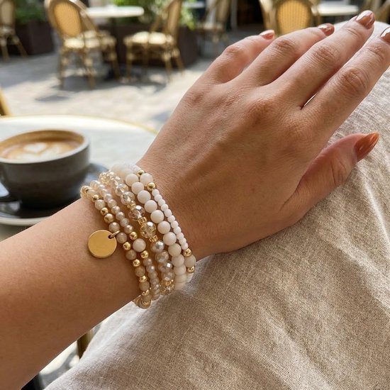 Damesarm met set van 5 witte en gouden armbanden, met ronde gouden bedel.