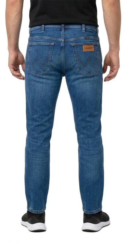 Achterkant van model in blauwe Wrangler slim fit spijkerbroek met bruin logolabel en W-stiksels.