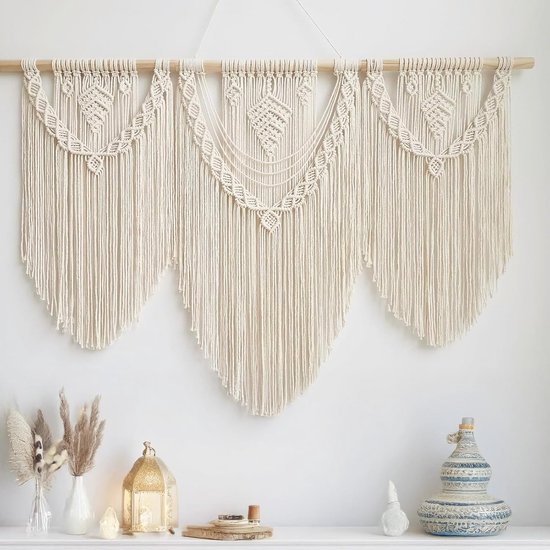 Macramé wandkleed in off-white met drie hangende secties, gedetailleerde knoopdetails en een houten stok.