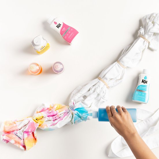 Wit T-shirt met tie-dye patronen in geel, roze en blauw, omringd door kleurstofflessen.