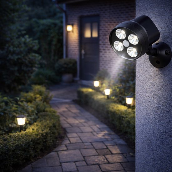 Zwarte buitenlamp met vier schijnende LED's verlicht een tuinpad bij een huis in de schemering.