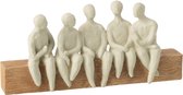 Vijf zittende, gebroken witte poppetjes van polyresin op een houten balk.