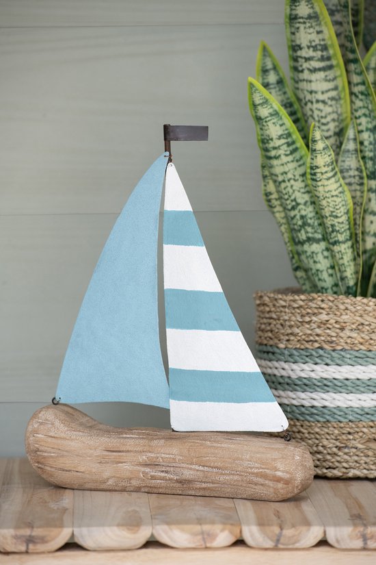Voilier décoratif en bois flotté avec voiles bleu clair et blanches rayées, à côté d'une plante dans un panier.