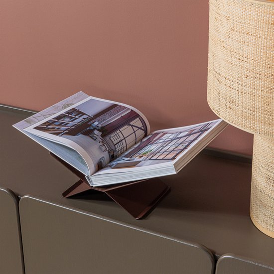 Een open boek met interieurfoto's staat op een bruine boekenstandaard, naast een lamp.